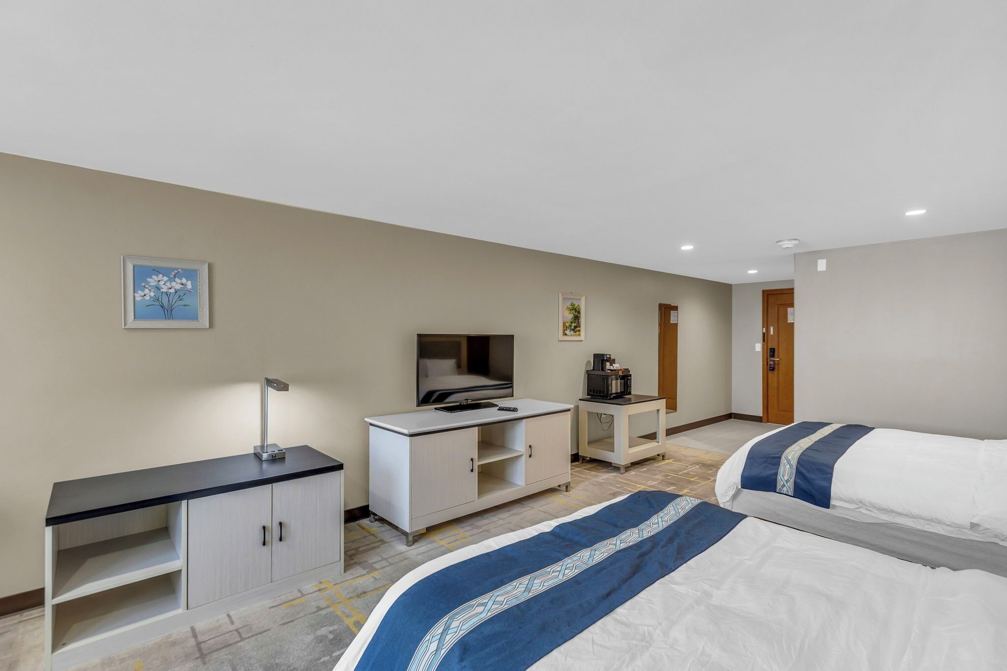 A hotel room with two beds, a desk, a chair, a coffee machine, and a TV.