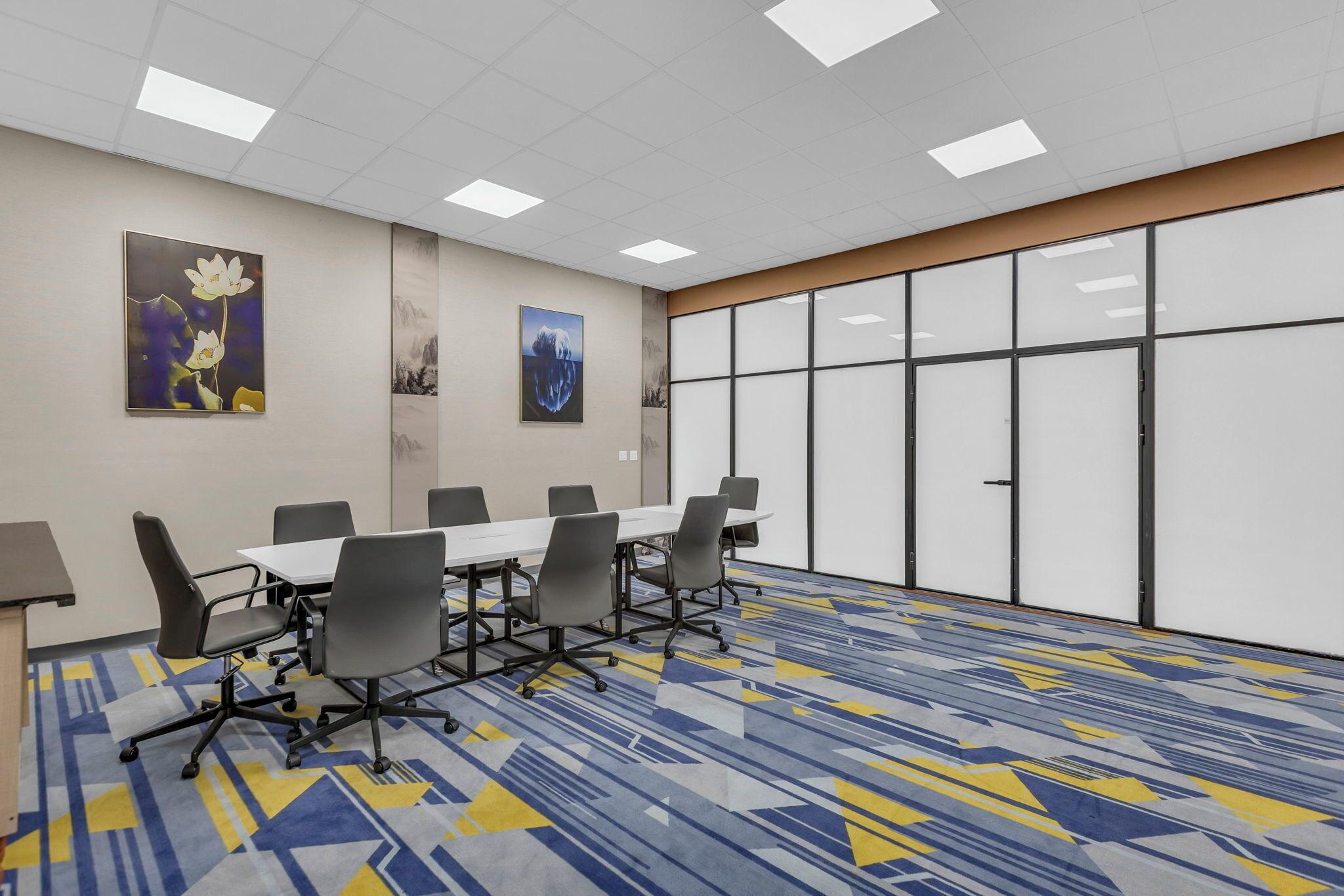 A conference room with a long table, six chairs, and a patterned carpet.