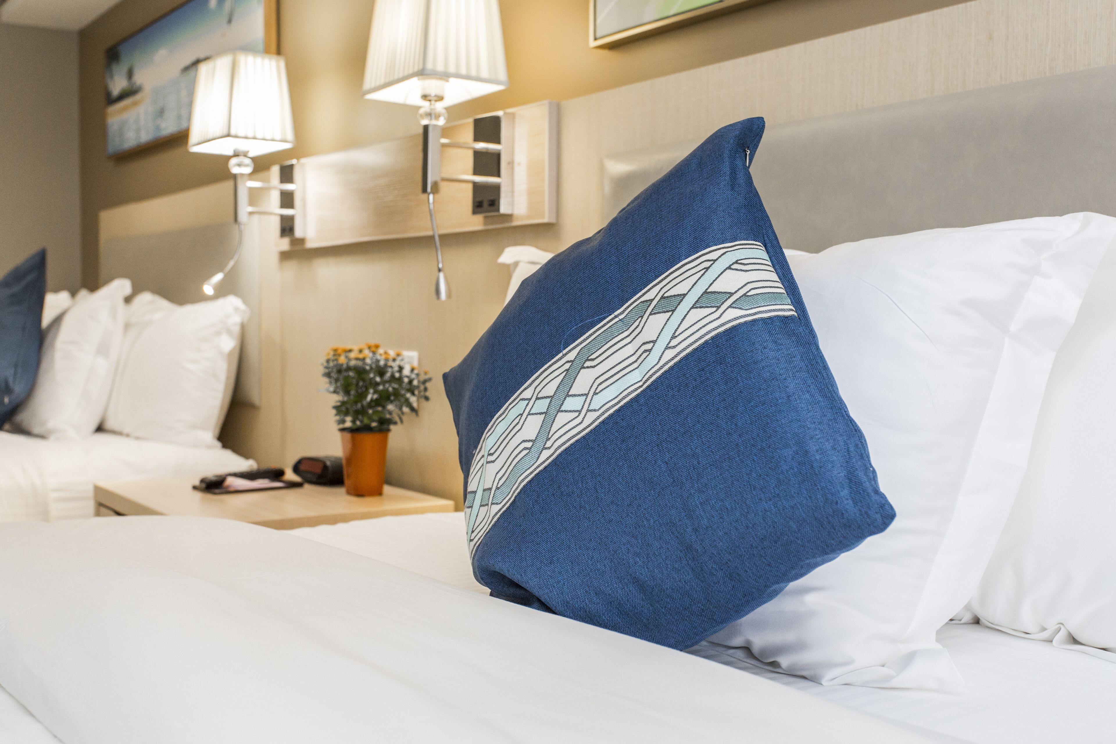 Una habitación de hotel con una cama bien hecha, una mesita de noche con lámpara y una pequeña planta en maceta.