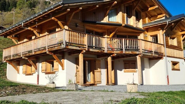 A wooden chalet with a balcony, set against a mountainous backdrop.