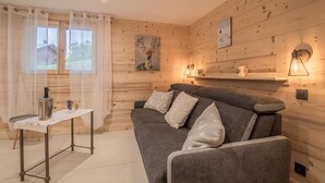 A cozy room with a grey sofa, a small table with a kettle, and two wall-mounted lamps.