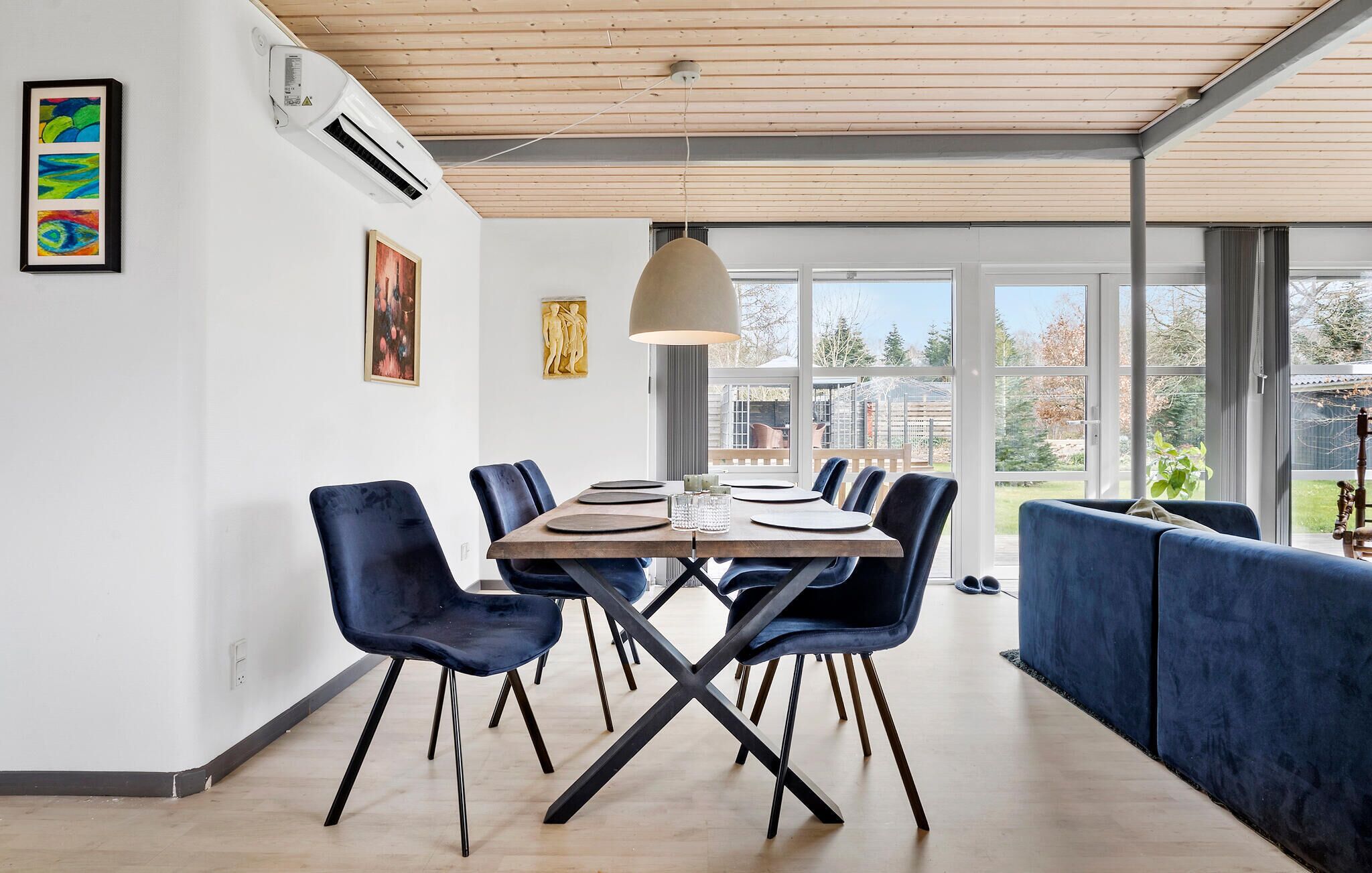 A modern dining area with a wooden table, blue chairs, and a large window offering a view of the outdoors.
