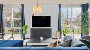 A modern living room with a large flat-screen TV, a sofa, a coffee table, and a potted plant. - 3 bedroom stunning home in Fårvang (Fårvang)