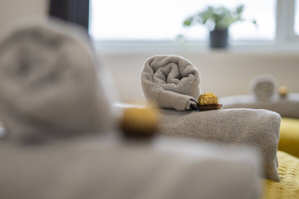 A neatly folded towel on a bed with a small chocolate bar and a bottle of lotion.