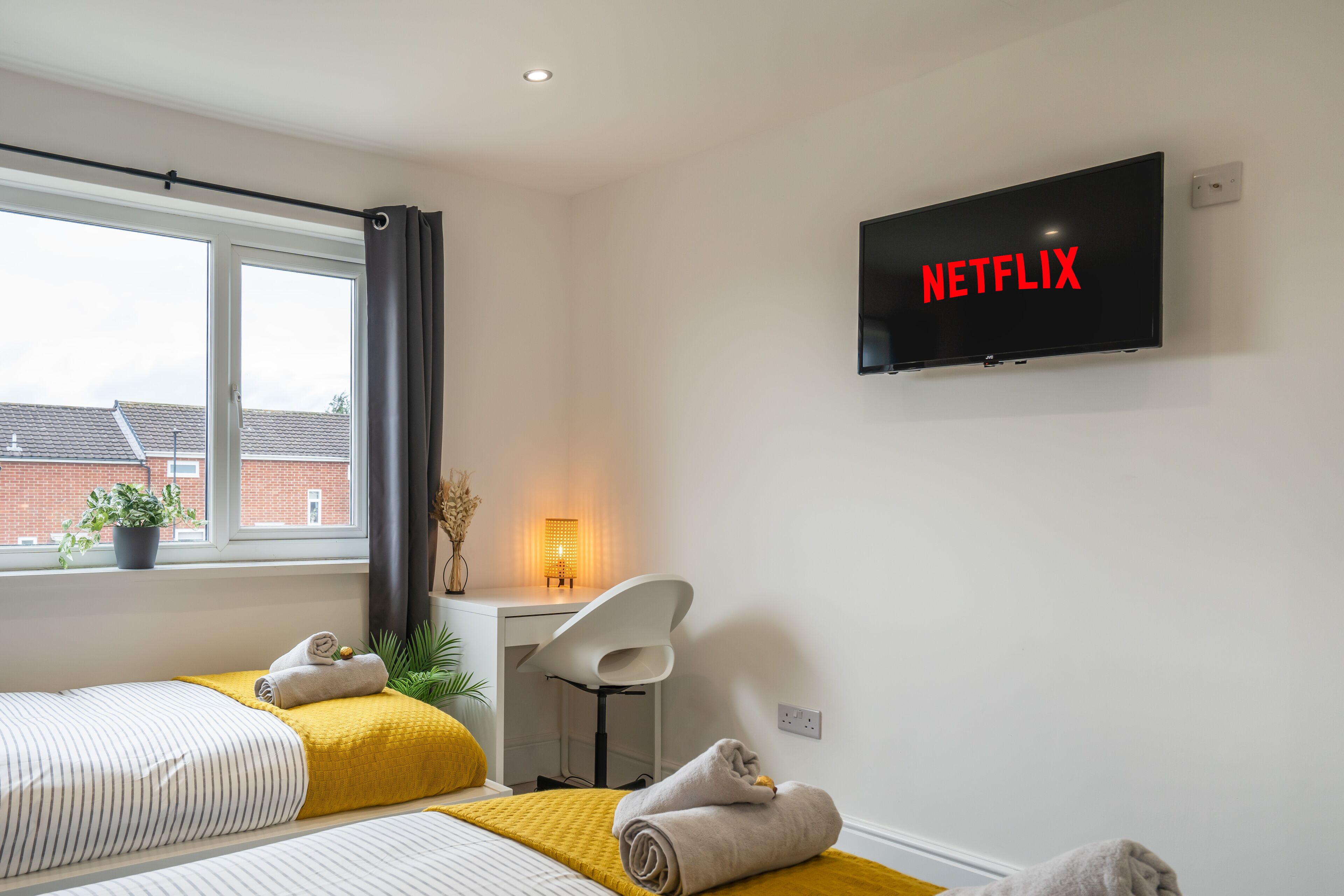 Een moderne hotelkamer met twee bedden, een bureau, een stoel en een televisie waarop 'NETFLIX' wordt weergegeven.