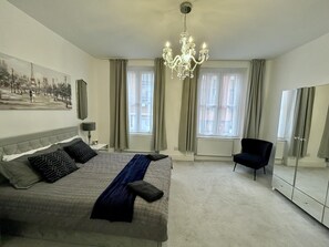 A bedroom with a large bed, a chandelier, a chair, and a wardrobe. - Apartment - Sleeps 4 & Near Tube (London)