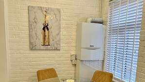 Een eetruimte met een glazen tafel en vier gele stoelen, een marmeren kunstwerk aan de muur, een witte airconditioning en een raam met jaloezieën.