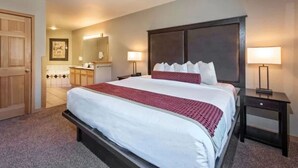 A hotel room with a large bed, two bedside tables, a wardrobe, and a bathroom visible through an open door.