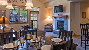 A dining area with a fireplace, a television mounted above it, and a view of the outside through large windows.