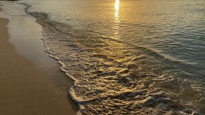 A beach with gentle waves and a setting sun.