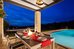 An outdoor dining area with a pool, stone pillar, and a view of the landscape.