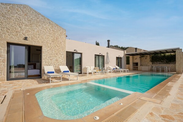 A swimming pool with lounge chairs and a stone building with glass doors.