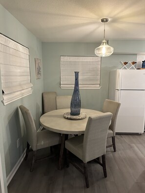 A dining area with a round table, four chairs, a blue vase, and a white refrigerator in the background. - Fun Crab Shack ~ 4 bedrm ~ 1 Block from Water (Rockport)