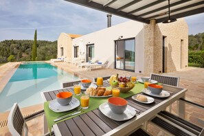 A poolside breakfast setup with a table, chairs, and a variety of food and drinks.