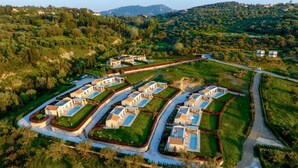 An aerial view of a residential area with multiple houses arranged in a grid pattern, surrounded by greenery and hills in the background. - Indulge in Opulence at Lithari Enac—Luxury Villa with Private Pool (Kavvadades)