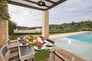 A dining table set with breakfast items, overlooking a swimming pool and scenic landscape.
