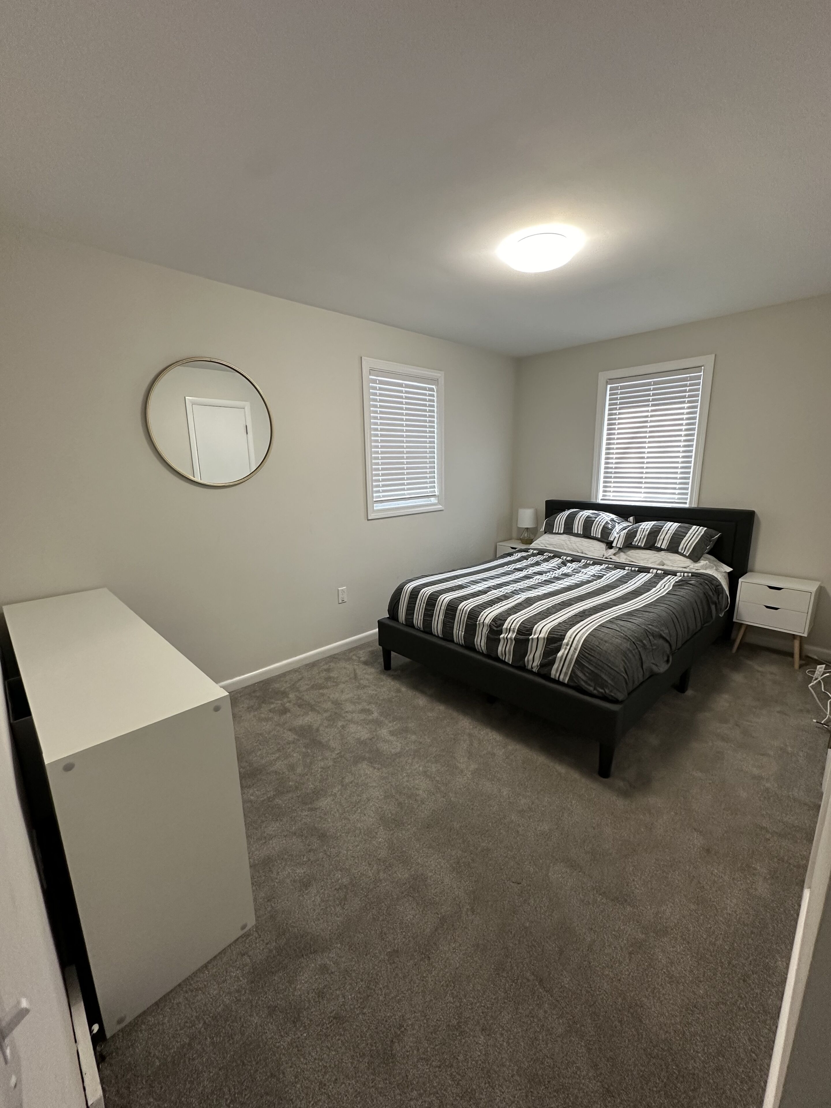 A bedroom with a bed, two bedside tables, a round mirror, and a wardrobe.