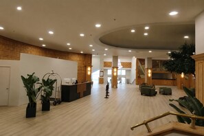 Een ruime lobby met een receptiebalie, een zithoek en een trap naar de verdiepingen erboven.