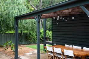 An outdoor patio with a wooden table and chairs, surrounded by a wooden fence and greenery. - Porpoise Palace - Huskisson (Huskisson)