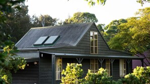 A dark wooden house with a sloped roof, a small porch, and a window with a wooden frame. - Porpoise Palace - Huskisson (Huskisson)