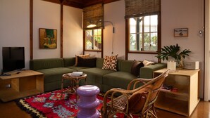 A cozy living room with a green sofa, a television, a small table, and a wicker chair. - Porpoise Palace - Huskisson (Huskisson)