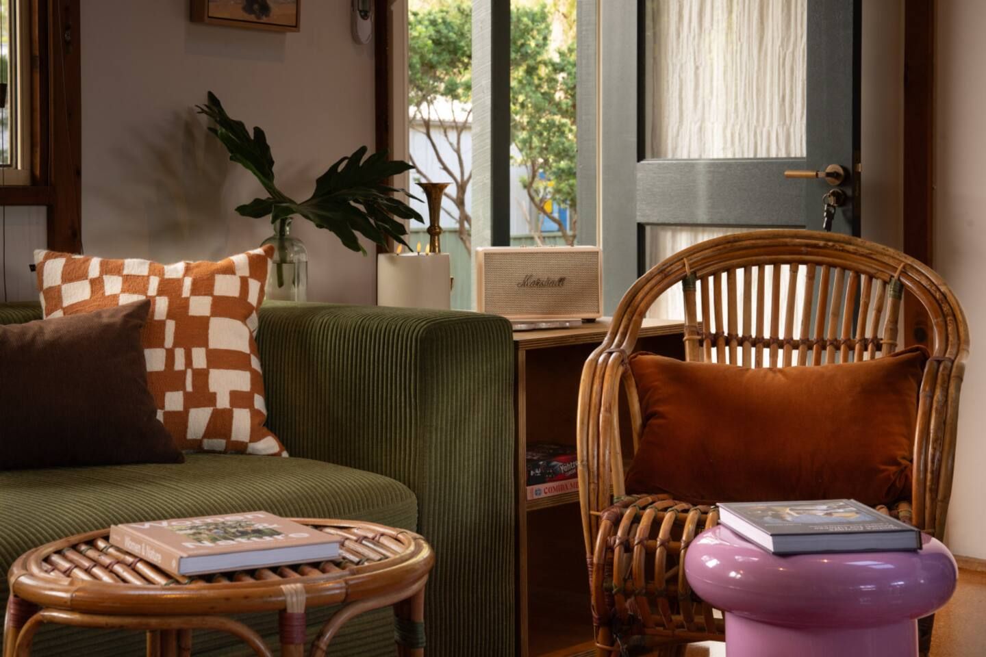 A room with a green sofa, a wicker chair, a small round table with a book, and a door with a curtain.