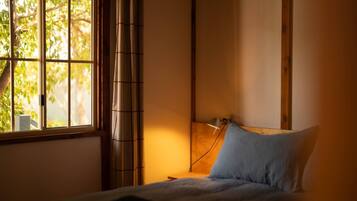 A bedroom with a bed, a bedside lamp, a window with curtains, and a view of trees outside.