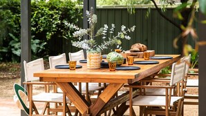 An outdoor wooden table set with chairs, surrounded by greenery and a wooden fence. - Porpoise Palace - Huskisson (Huskisson)