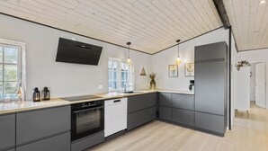 A modern kitchen with a built-in oven, dishwasher, and a large island with a sink. There are pendant lights above the island and a flat-screen TV mounted on the wall. - 3 bedroom amazing home in Vejby (Vejby)