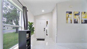 Un couloir avec une porte blanche, une plante et des œuvres d’art accrochées au mur.