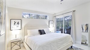 Une chambre à coucher avec un grand lit, une table de chevet, un ventilateur de plafond et une fenêtre donnant sur l’extérieur.