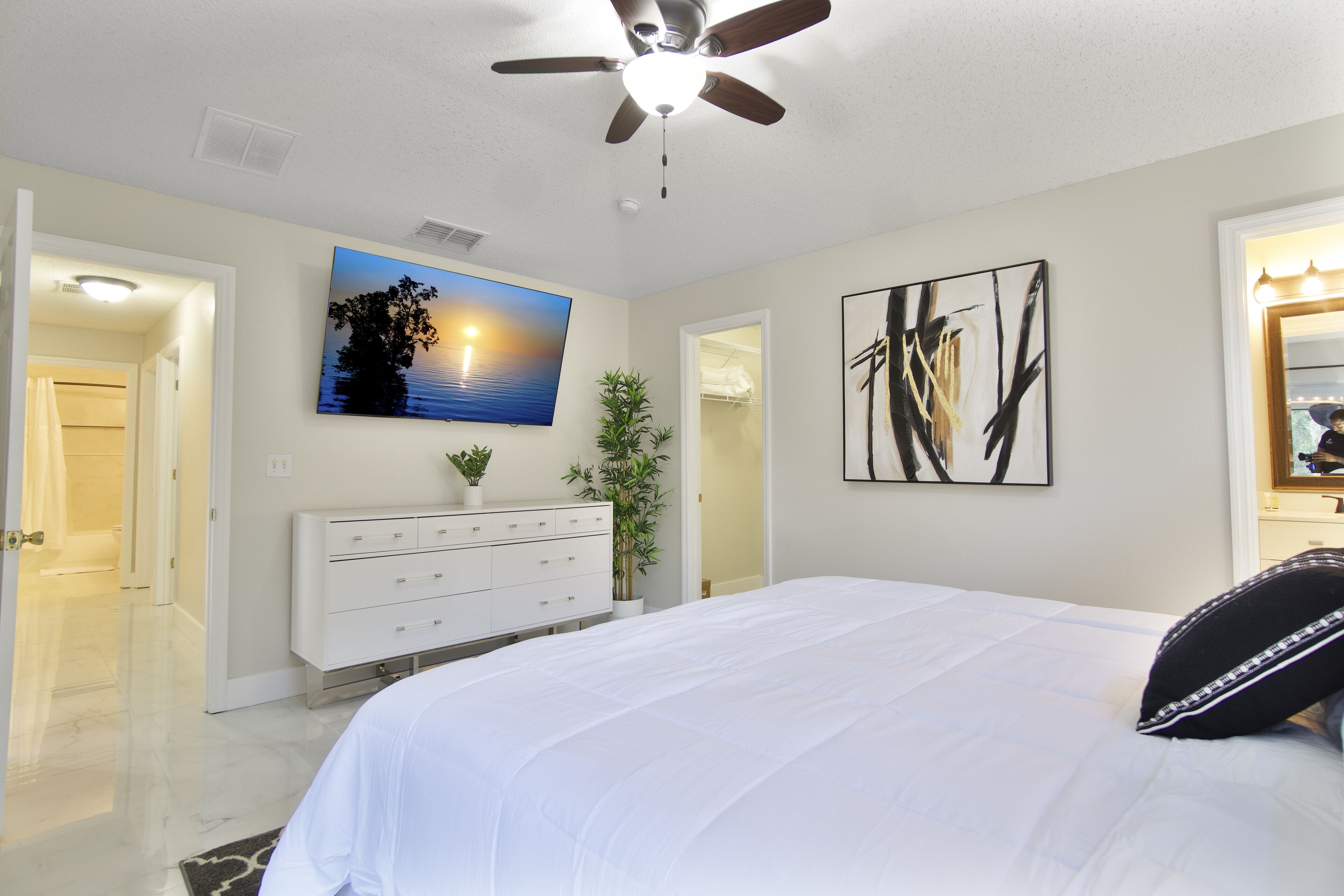 A bedroom with a bed, a ceiling fan, a TV, a dresser, and artwork on the walls.