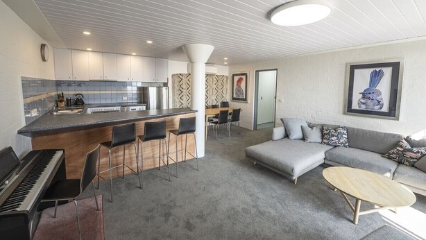 Eine moderne Küche mit Kochinsel, Barhocker, Essbereich und Wohnzimmer mit Sofa und Couchtisch.