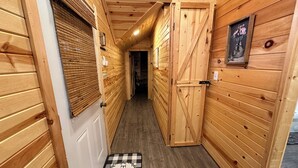 A narrow wooden hallway with a door at the end, a checkered mat with "HOME" in the center, and a framed picture on the right wall.