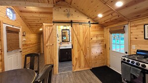 A wooden cabin interior with a kitchen, dining area, and a large sliding door leading to a bathroom.