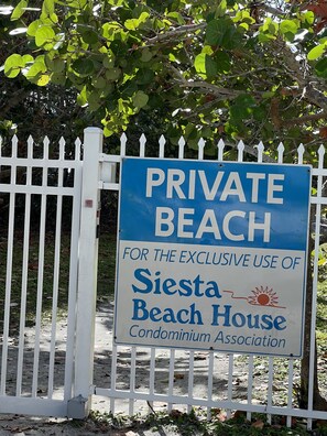 Une pancarte sur une clôture blanche indique : « PLAGE PRIVÉE RÉSERVÉE À L’USAGE EXCLUSIF DES MEMBRES DE L’ASSOCIATION DES COPROPRIÉTAIRES DE SIesta Beach House. »