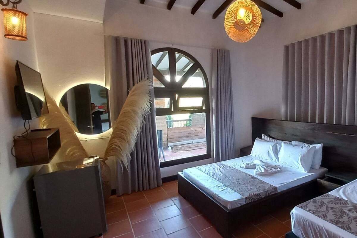 A hotel room with a bed, a sofa, a TV, and a window with curtains.