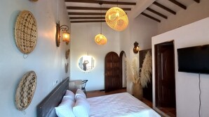 A bedroom with a bed, wall-mounted TV, woven wall decorations, and a ceiling fan. - Hotel Ecoluxe (El Peñol)