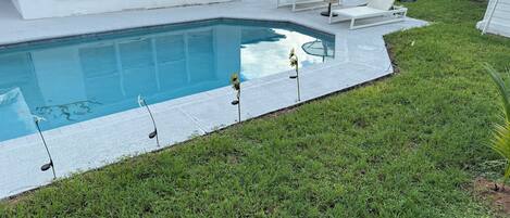 A swimming pool with a tiled deck, surrounded by a grassy lawn and a white fence.
