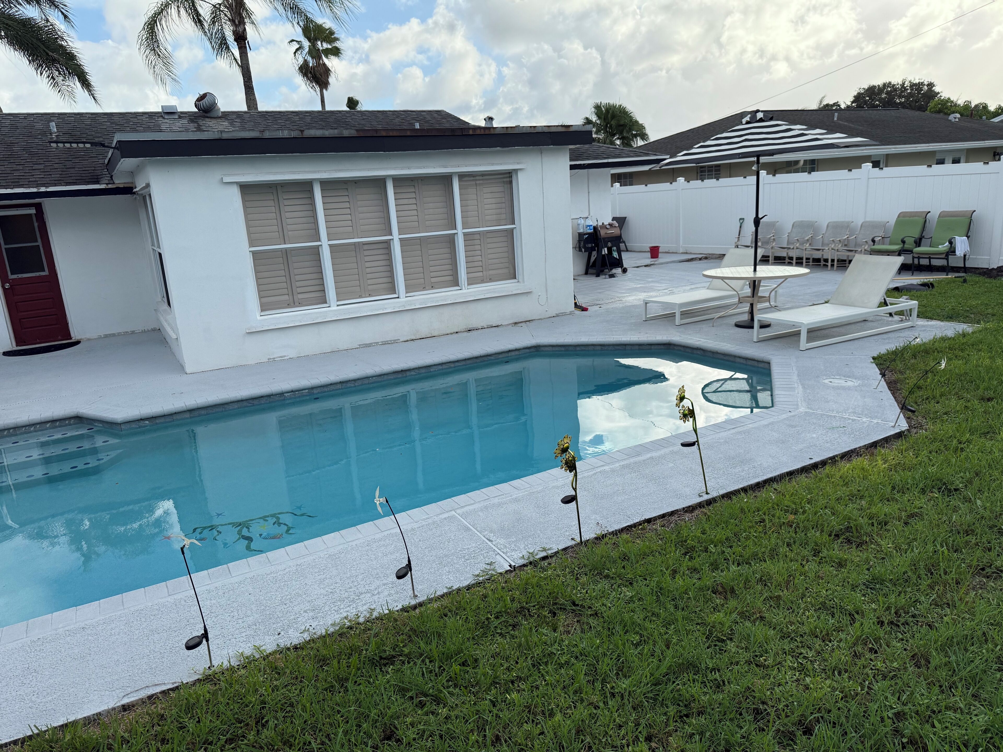Ein Swimmingpool mit einem weißen Haus und Terrassenmöbeln.