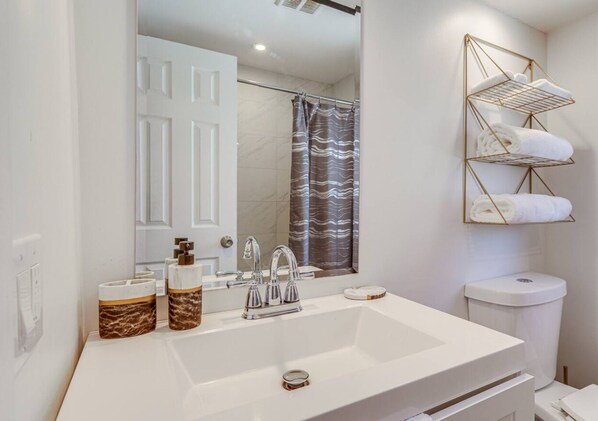 A bathroom with a large mirror, white sink, and a towel rack with folded towels. - Prime Location w/pool (Palm Beach Gardens)