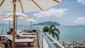 A deck with sun loungers and umbrellas overlooking a calm sea with distant islands. - Malee Resort Studio 858 (Rawai)