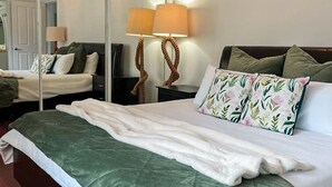 A neatly made bed with a green and white duvet, a white bathrobe draped over the side, and a lamp with a twisted base.
