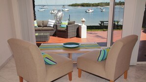 A room with two beige armchairs, a glass table, and a view of boats on the water.
