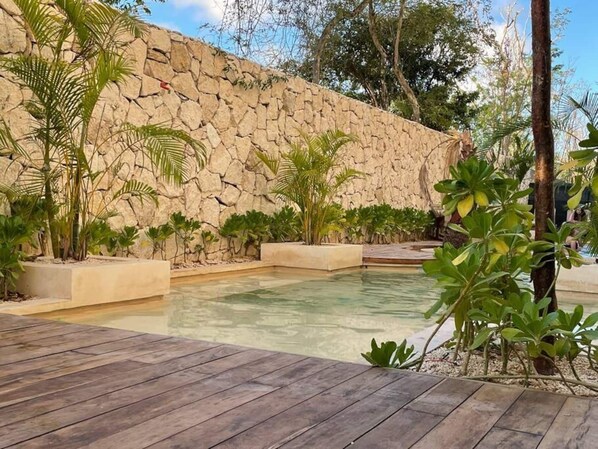 A pool area with a stone wall, surrounded by various plants and a wooden deck.