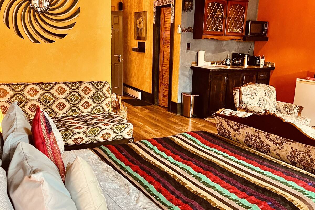 A cozy room with a large bed, patterned pillows, a colorful striped rug, and a wooden ceiling.