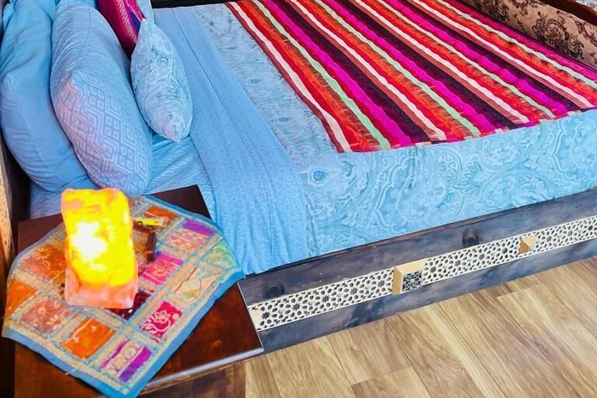 A room with a bed, a patterned headboard, a colorful striped rug, and a small table with a candle.