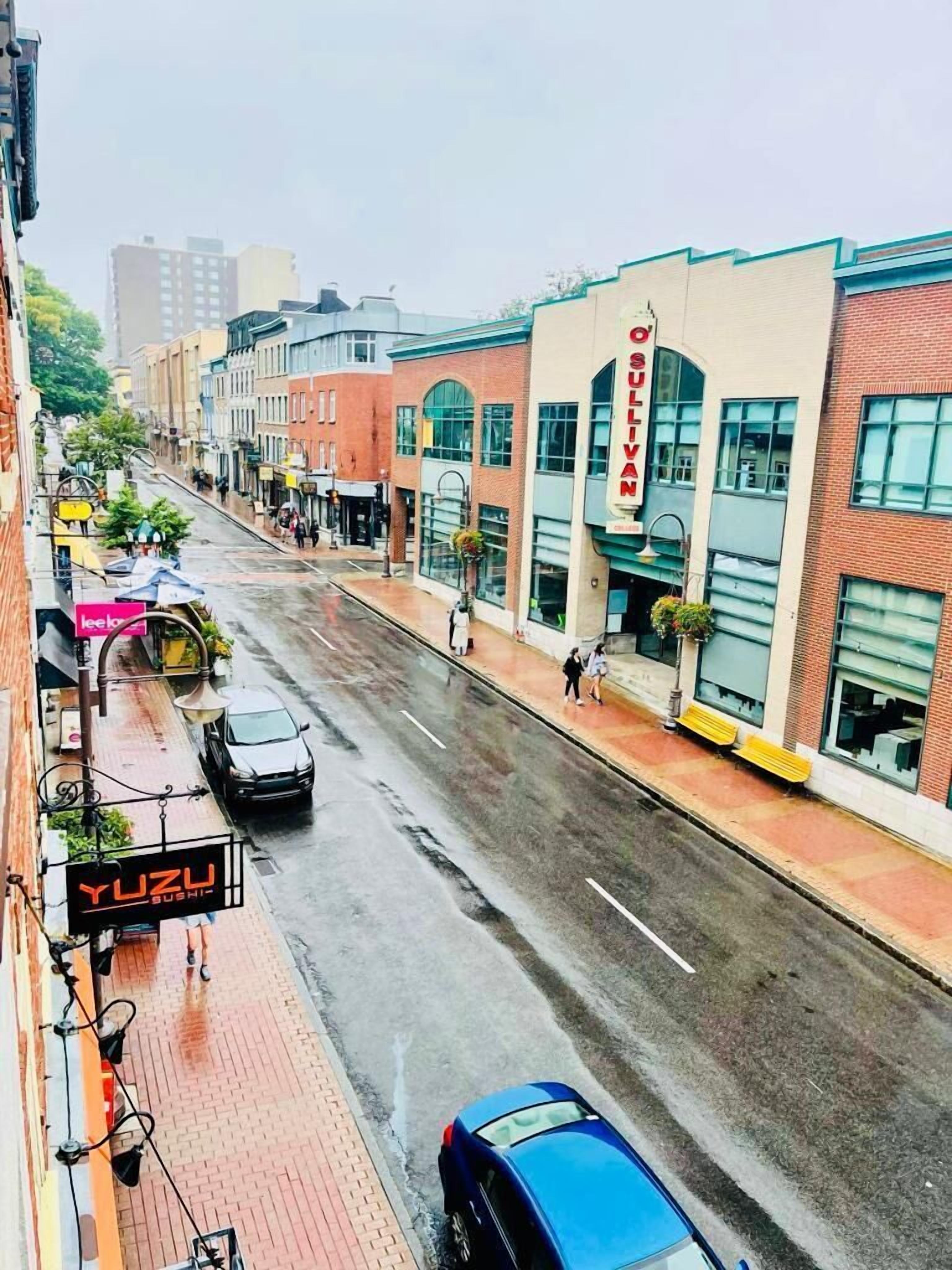 A street view with a sushi restaurant, a blue car, and a building with a sign that reads 'O'SULLVAN'.