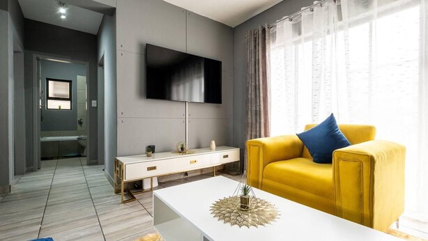 Una sala de estar moderna con un sofá amarillo, una mesa de centro blanca y un televisor de pantalla plana montado en la pared.
