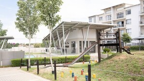 Un edificio moderno con un espacio exterior cubierto, una escalera y un parque infantil.